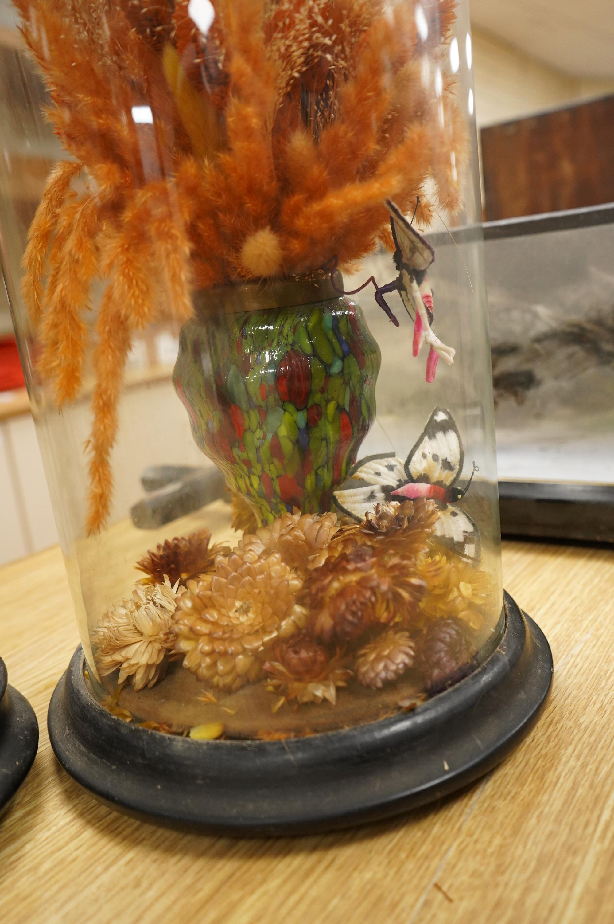Two Victorian fauna displays under domes with ebonised bases, containing dried grasses and flowerheads, together with fabric butterflies, tallest 46cm, both af